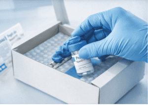 Hand in blue glove handling peptide vial in lab setting.